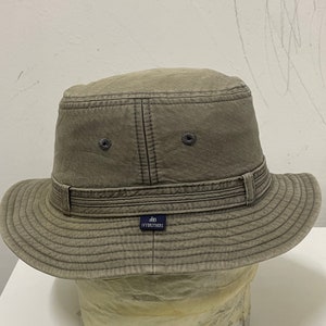 May include: A gray canvas bucket hat with a brown leather band and a navy blue label that reads "Ivy Brothers".