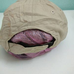 May include: A beige baseball cap with a black brim and a pink mesh lining. The cap is folded in half and the lining is visible.