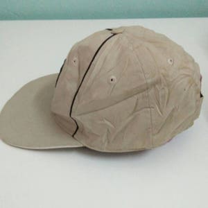 May include: A beige baseball cap with a black stripe and a textured design. The cap has a curved brim and a mesh back.