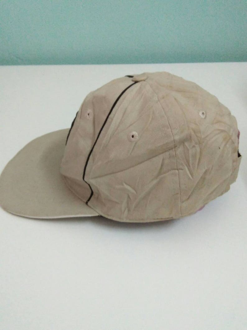 May include: A beige baseball cap with a black stripe and a textured design. The cap has a curved brim and a mesh back.
