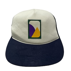 May include: A white and navy blue trucker hat with a green, yellow, and purple geometric design on the front.
