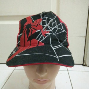 May include: A black and red baseball cap with a spider-man design. The cap has a mesh back and a red brim.