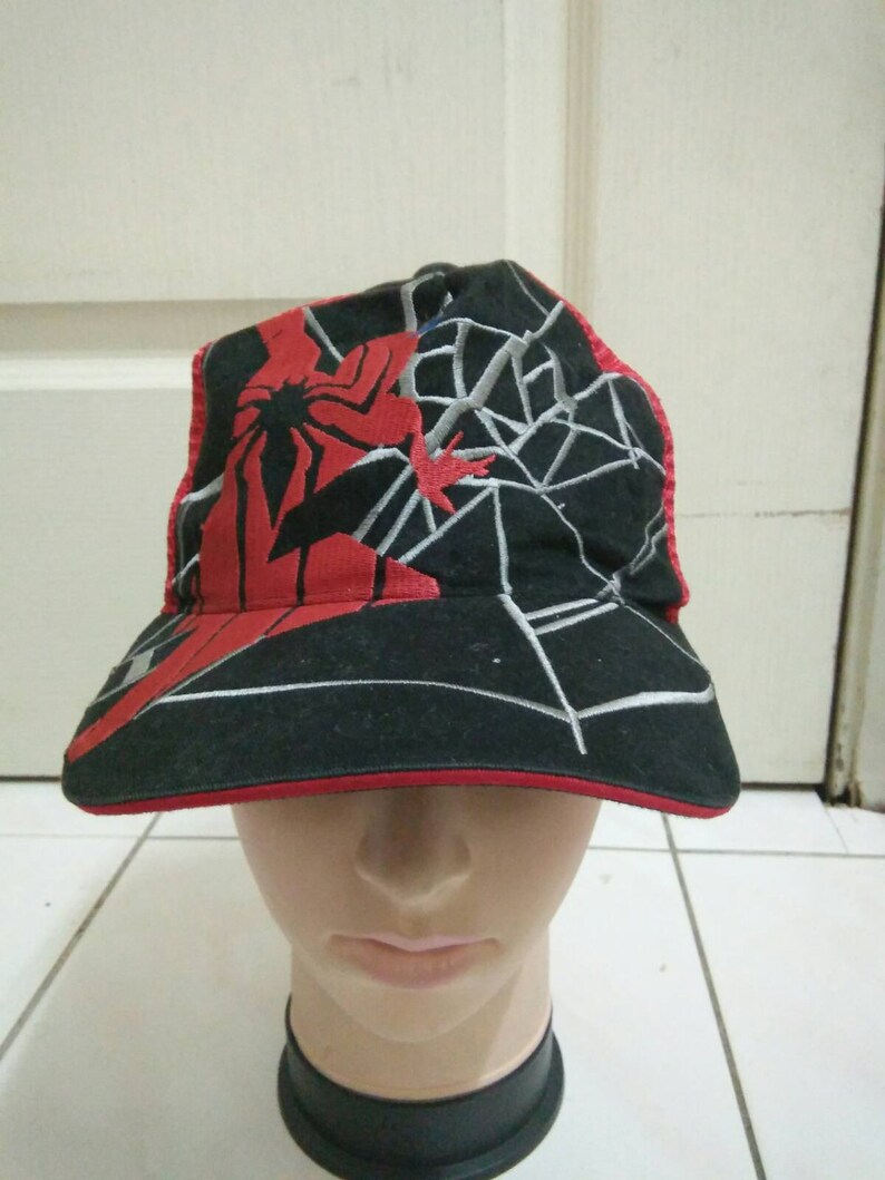 May include: A black and red baseball cap with a spider-man design. The cap has a mesh back and a red brim.
