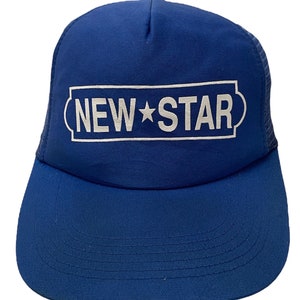 May include: A blue trucker hat with a white rectangular logo that reads "NEW STAR" with a star graphic. The hat has a mesh back and a curved brim.