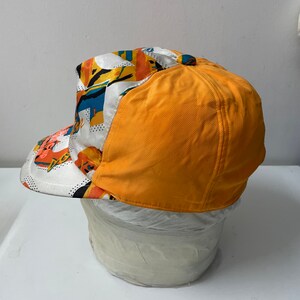 May include: A yellow and white baseball cap with a colorful abstract pattern. The cap has a curved brim and a structured crown.