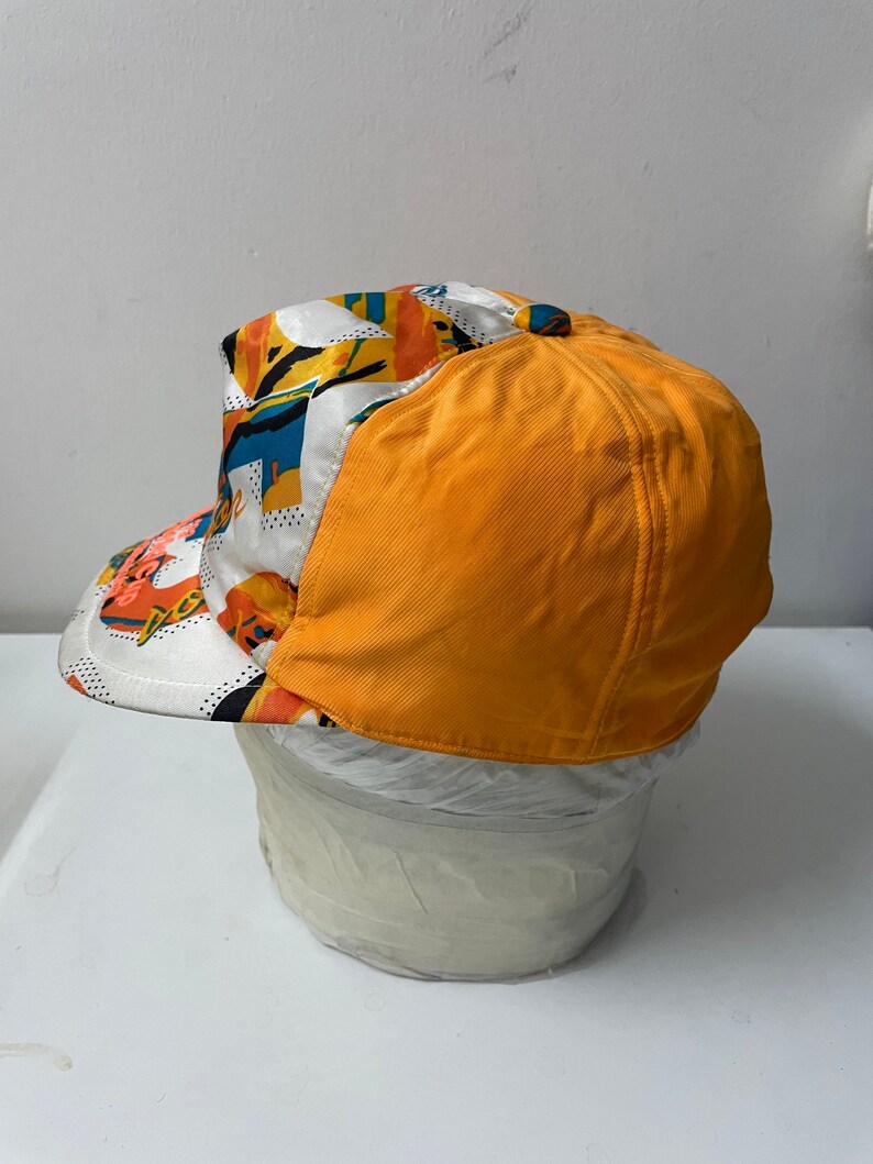May include: A yellow and white baseball cap with a colorful abstract pattern. The cap has a curved brim and a structured crown.