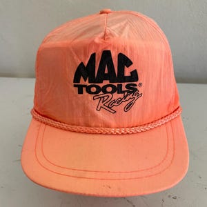 Könnte beinhalten: Korallenfarbene Baseballkappe mit dem schwarzen Text "MAC TOOLS Racing". Die Kappe hat eine Kordel um den Rand und einen gebogenen Schirm. Der Hut ist aus leichtem Material gefertigt.