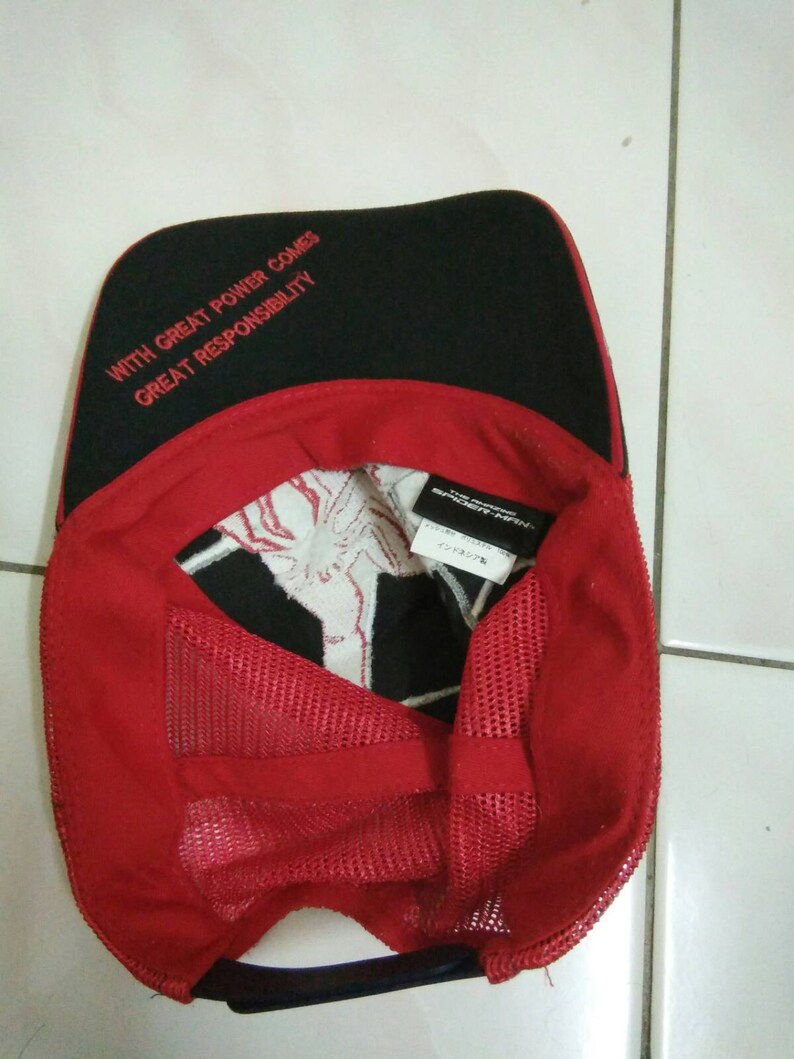 May include: A red and black baseball cap with a mesh back. The front of the cap has the text "With great power comes great responsibility" embroidered in red. The back of the cap has a white tag with black text.