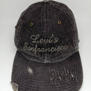 May include: A black denim baseball cap with a distressed look. The cap has a gold metal eyelet on each side and the text "Levi's San Francisco" embroidered on the front in a light gray thread.