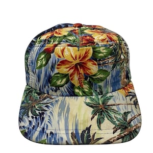 Può includere: Un cappello da baseball con stampa tropicale blu, gialla e verde con palme e fiori di ibisco.