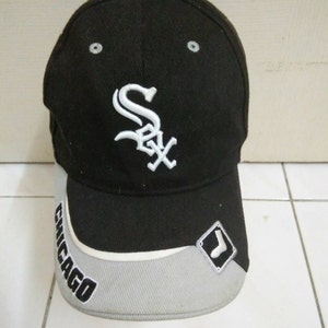 May include: Black baseball cap with a white "Sox" logo and a white "Chicago" inscription on the brim. The cap also has a white diamond-shaped patch with a white sock logo on the side.