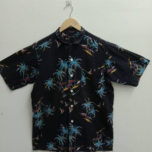 May include: A black short-sleeved button-down shirt with a palm tree print. The shirt has a collar and a button closure. The brand name "Jolly King" is printed on the collar.
