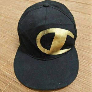 May include: Black baseball cap with a gold embroidered Champion logo.