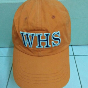 May include: An orange baseball cap with a white and blue embroidered logo that says "WHS".