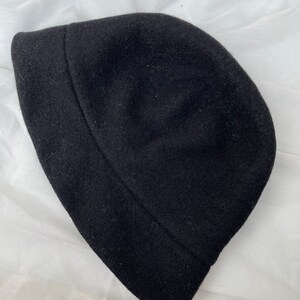 May include: A black felt bucket hat. The hat is made of a soft, textured fabric.