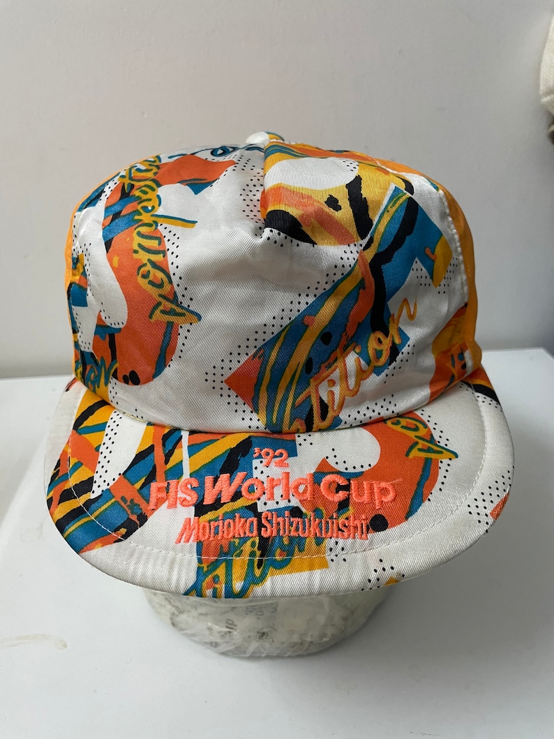 May include: White baseball cap with a colorful abstract print and the text "FIS World Cup '92 Morioka Shizukuishi" embroidered in orange.