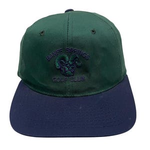 May include: A green and blue baseball cap with the text "Banff Springs Golf Club" and a ram's head logo embroidered on the front.