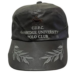 May include: A black leather baseball cap with a brown embroidered logo that reads "C.U.P.C. CAMBRIDGE UNIVERSITY POLO CLUB" and a silver embroidered laurel wreath on the brim.