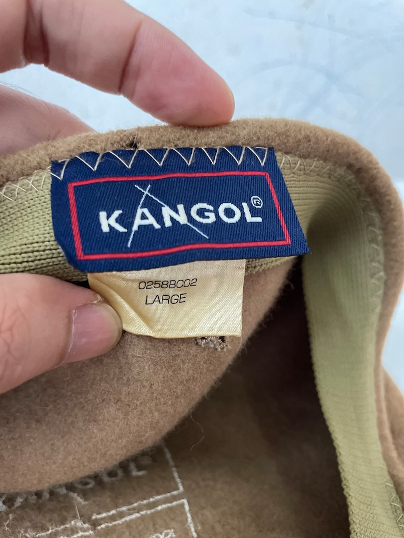 以下が含まれることがあります： Kangolのロゴと「0258BC02 LARGE」のラベルが付いた茶色の帽子。
