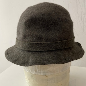 May include: A dark grey felt bucket hat with a brown leather band around the crown.