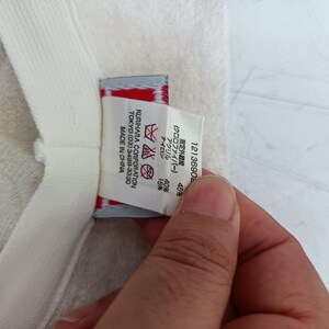May include: A cream-colored textured hat featuring an interior white fabric label with black text. The label displays care instructions, the manufacturer name Kurihara Corporation, Tokyo, and material composition percentages of 45%, 40%, and 15%.