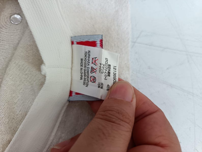 May include: A cream-colored textured hat featuring an interior white fabric label with black text. The label displays care instructions, the manufacturer name Kurihara Corporation, Tokyo, and material composition percentages of 45%, 40%, and 15%.