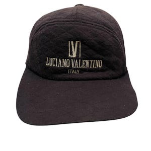 May include: A black baseball cap with a gold embroidered logo that reads "Luciano Valentino Italy".