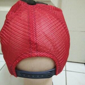 May include: Red mesh trucker hat with a black brim and a black adjustable strap in the back.