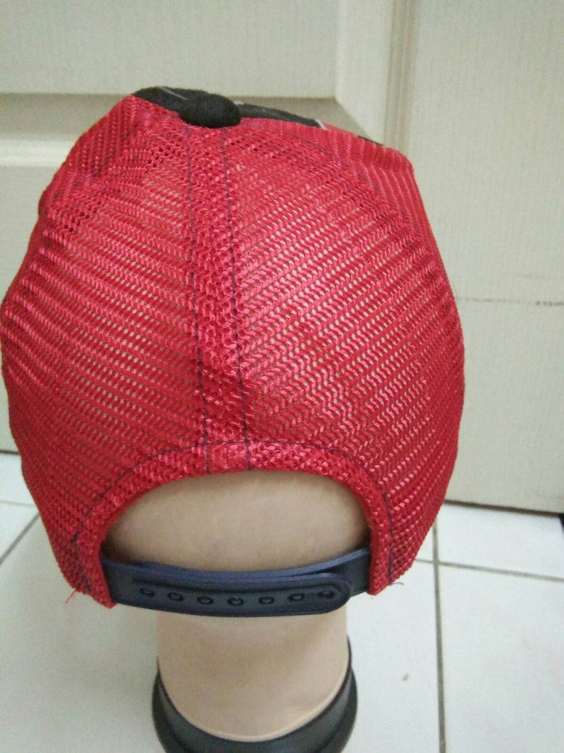 May include: Red mesh trucker hat with a black brim and a black adjustable strap in the back.