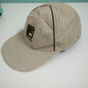 May include: A beige baseball cap with a black Fila logo embroidered on the front.
