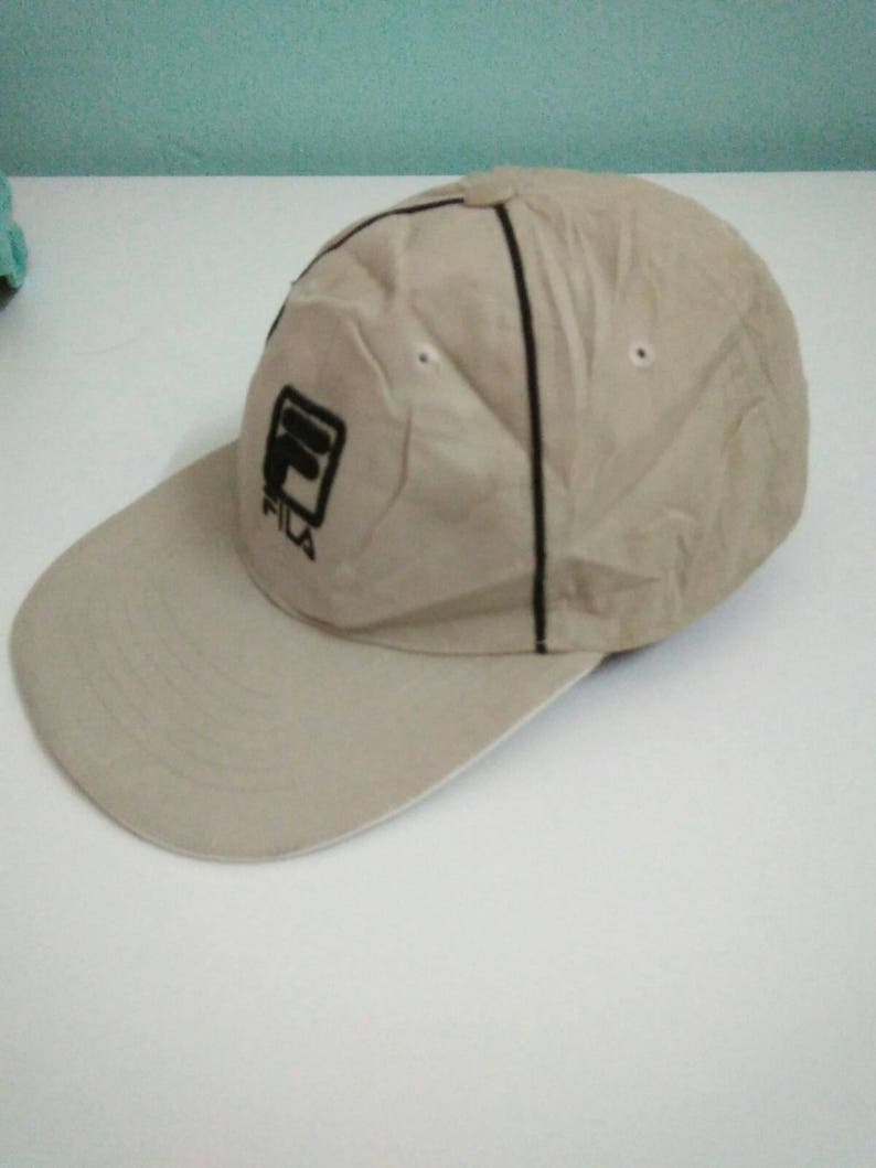 May include: A beige baseball cap with a black Fila logo embroidered on the front.