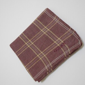May include: A red and tan plaid handkerchief with the word "GUESS" embroidered in white.