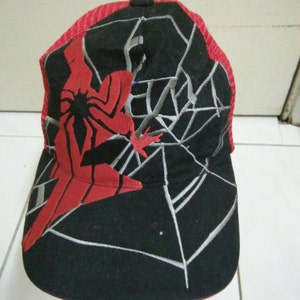 May include: Black and red baseball cap with a spider web design and a red Spiderman figure. The cap has a mesh back.