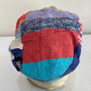Op de afbeelding: Een veelkleurige patchwork hoed. De hoed is gemaakt van verschillende geweven stoffen in tinten rood, blauw, paars en oranje. Een uniek, handgemaakt accessoire.