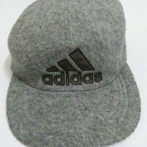 May include: A gray fleece baseball cap with a black Adidas logo. The logo is a stylized three-leaf clover with the word "adidas" written below it.