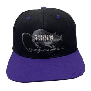 May include: Black and purple baseball cap with a gray embroidered rat and the text "Storm Brewing Co. Est. 1994 Vancouver, BC."