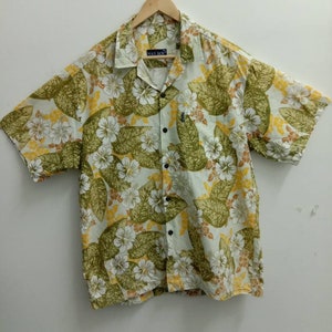 Op de afbeelding: Een wit, kort mouwig overhemd met knopen en een groene, gele en bruine bloemenprint. Het overhemd heeft een kraag en een knoopsluiting. De merknaam "MAX BOY" is op de voorkant van het overhemd gedrukt.