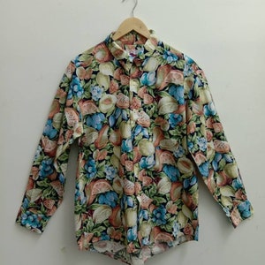 May include: A long-sleeved button-up shirt with a colorful fruit print. The shirt has a white background with a variety of fruits, including oranges, lemons, pears, and watermelons.
