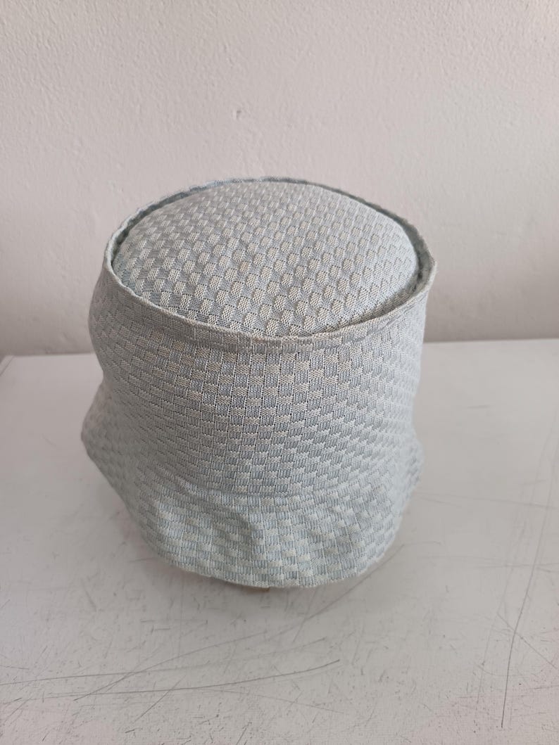 May include: A light blue and white bucket hat featuring a textured, woven checkerboard pattern throughout the crown and the brim. The hat has a rounded top and a downward-sloping brim, constructed from a soft, flexible fabric with a consistent grid design.