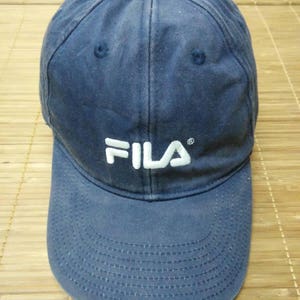 May include: A blue baseball cap with a white FILA logo embroidered on the front.