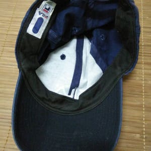 May include: A navy blue baseball cap with a black brim and a white label with the word "FILA" in black lettering.