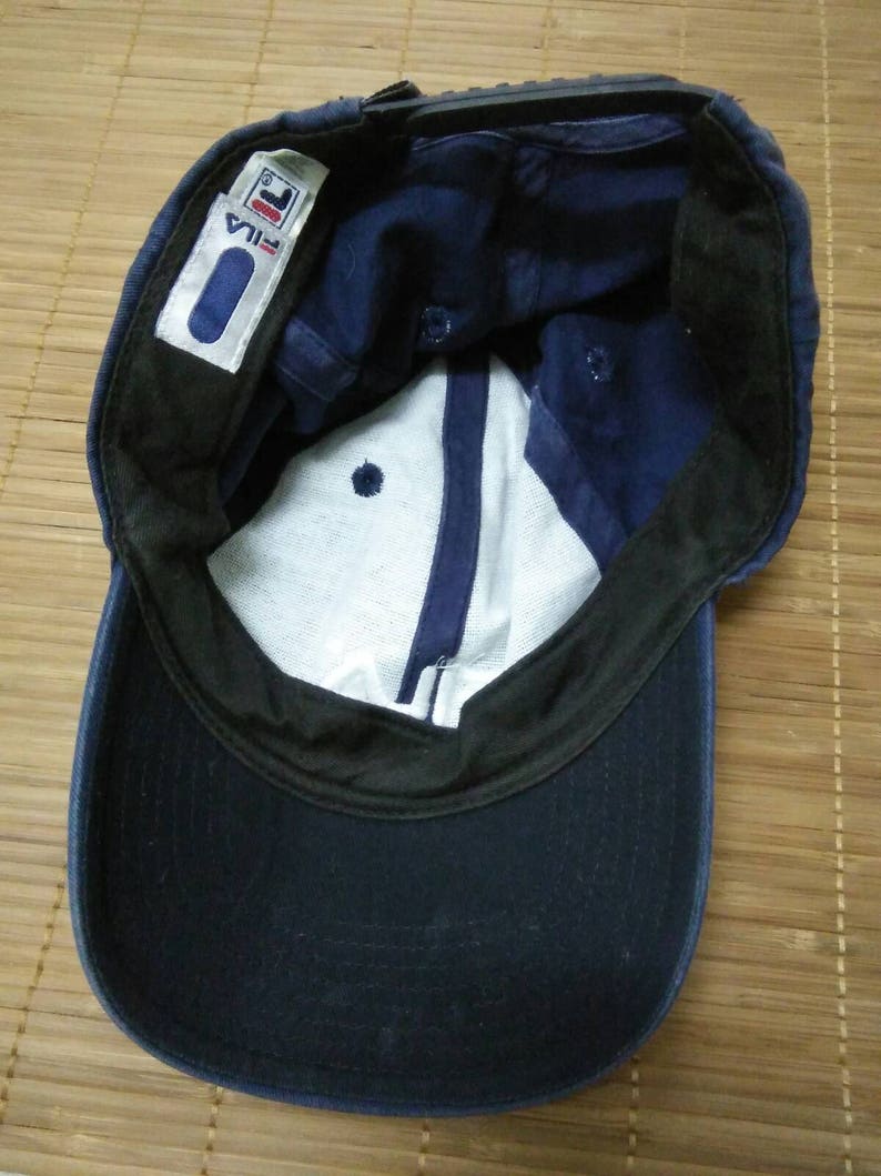 May include: A navy blue baseball cap with a black brim and a white label with the word "FILA" in black lettering.