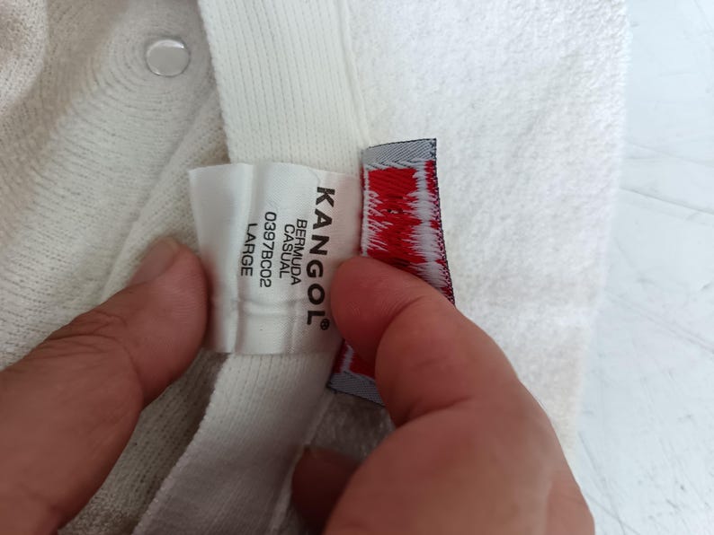May include: A white Kangol Bermuda Casual bucket hat with a textured fabric finish. The interior label displays the brand name Kangol, the style name Bermuda Casual, the code 0397BC02, and the size Large in black text on a white background.