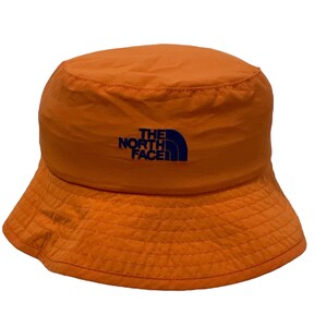 May include: An orange bucket hat with a navy blue "THE NORTH FACE" logo embroidered on the front.