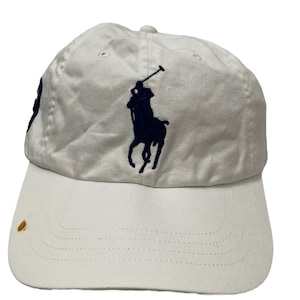 May include: White baseball cap with a navy blue embroidered polo player logo.