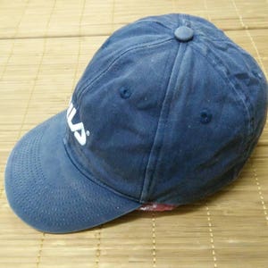 May include: A blue baseball cap with a white Fila logo embroidered on the front. The cap has a slightly distressed look.