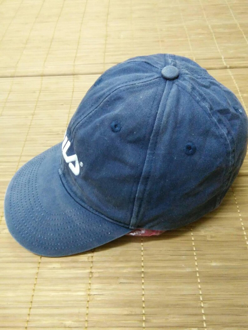 May include: A blue baseball cap with a white Fila logo embroidered on the front. The cap has a slightly distressed look.