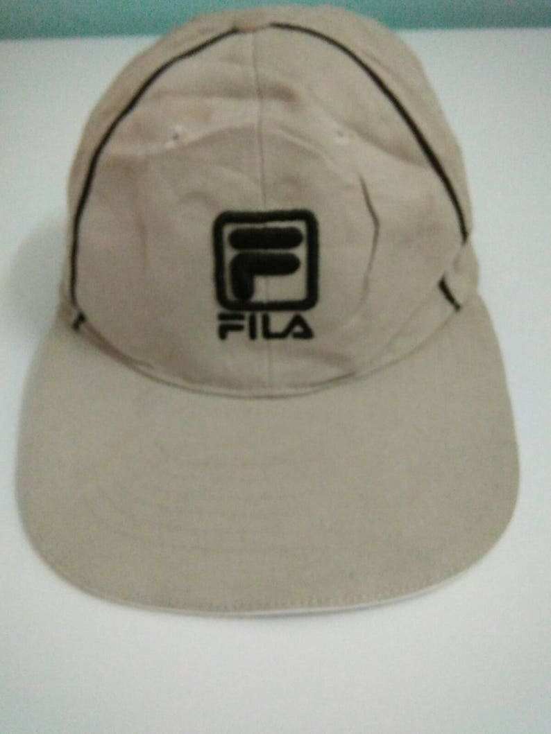 May include: A beige baseball cap with a black Fila logo on the front.