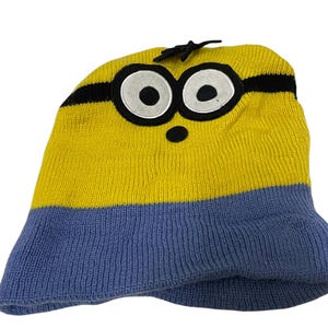May include: Yellow and blue knitted beanie hat with a black stripe and a felt Minion face with large eyes.