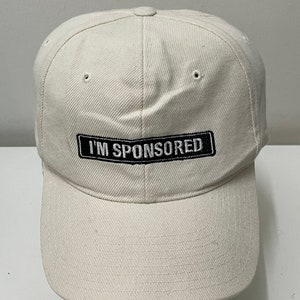 May include: A white baseball cap with a black patch that says "I'M SPONSORED" in white lettering.